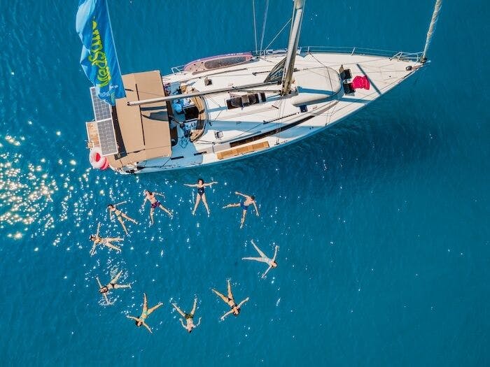 Photo of group of people swimming in a star shape near a sailing yacht in the Mediterranean. 